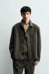 Sobrecamisa de corte regular fit en tejido elástico y transpirable, con cuello solapa, cierre frontal mediante botones a presión y bolsillo de plastrón en el pecho. Presenta mangas largas con puños abotonados y bajo con aberturas laterales.