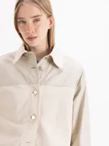 Camisa de manga larga color beige con diseño combinado, que incluye panel frontal de tejido texturizado, cuello clásico y cierre frontal de botones.