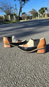 Zapatos de cuero estilo mocasín con taco bajo de madera, diseño multicolor en tonos negro charol, tostado, beige y marrón, con detalles elásticos laterales.