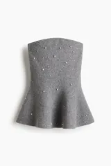 Top strapless de tejido de punto gris, ajustado al cuerpo con peplum acampanado en la parte inferior. Está adornado con perlas y pequeños cristales distribuidos por toda la prenda.