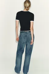 Camiseta blanca de manga corta y cuello redondo, con ribete negro decorado con perlas blancas en el cuello y los puños.