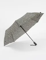 Paraguas plegable automático con funda protectora estampada con diseño floral en tonos rojos, blancos y amarillos. Cuenta con mango ergonómico negro y correa de sujeción.