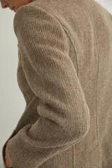 Saco corto entallado de lana fina, con cuello solapa, manga larga y cierre frontal con botones. Presenta un diseño clásico con textura de espiga en tonos tierra.