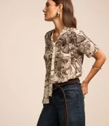 Blusa de chiffon con estampado de serpiente en tonos beige y marrón. Tiene cuello alto con lazo y mangas cortas.