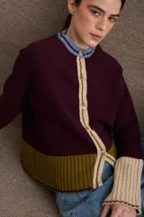Cardigan de punto con diseño color block en tonos bordó, verde oliva y beige. Presenta cuello redondo con detalle en celeste, cierre frontal con botones y puños acampanados en color beige.