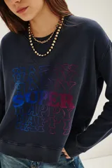 Buzo de cuello redondo y manga larga, en color azul oscuro con efecto lavado. Presenta un estampado frontal con la palabra 'HAPPY' repetida en un degradado de colores vibrantes.