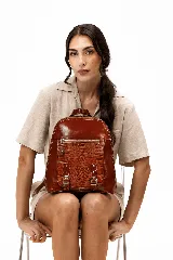 Mochila de cuero vacuno color marrón, con diseño estructurado y combinación de textura croco en el bolsillo frontal. Cuenta con un compartimento principal con cierre, un bolsillo frontal con cierre metálico y hebillas decorativas, y correas regulables.
