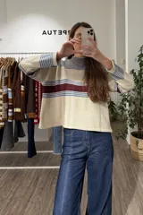 Sweater de punto corto con diseño a rayas horizontales en tonos beige, azul y bordó, cuello redondo y mangas largas con hombros caídos.