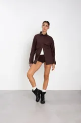 Botas de caña baja en cuero sintético color marrón, con diseño de estilo biker que incluye dos correas horizontales con hebillas metálicas y una argolla decorativa en el lateral. Posee suela y taco bajo de color negro.