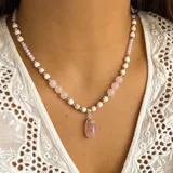 Collar de cuentas con dije colgante de cuarzo rosa pulido en forma de lágrima. El collar está compuesto por cuentas de cuarzo rosa de 8 mm, cuentas de piedra reconstituida de 6 mm y pequeñas cuentas metálicas plateadas.