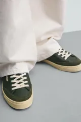 Zapatilla deportiva de estilo retro con diseño de paneles en cuero sintético color verde oscuro, detalles en crema y suela de goma en contraste.