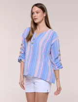 Blusa Erika de algodón con estampado de rayas en tonos azules, rosados y amarillos. Presenta cuello redondo con escote en V y botones frontales, mangas cortas decoradas con una fila de botones en los laterales y dobladillo asimétrico.