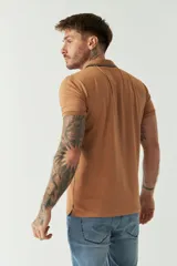 Remera polo de manga corta color tostado, con cuello clásico, cierre frontal de botones y un pequeño bolsillo en el pecho con logo estampado.