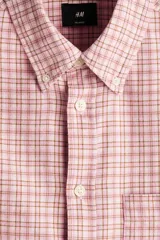 Camisa de sarga de algodón de corte relajado, con estampado a cuadros en tonos rosados y blancos, cuello americano, manga larga con puños abotonados y un bolsillo frontal en el pecho.