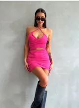 Minivestido fucsia con escote halter cruzado, espalda descubierta y falda ajustada con frunces.