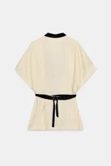 Kimono Zara Woman Collection de manga corta y cuello en V, confeccionado en tejido color crudo con sutiles rayas verticales. Presenta aplicaciones de terciopelo negro a contraste en la solapa y un fajín ancho integrado en la cintura.