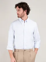 Camisa de hombre con diseño de rayas finas celestes y blancas, corte regular fit, cuello button down y manga larga. Cuenta con cierre frontal de botones y sutil logo bordado en el pecho.