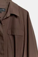 Vestido midi de estilo camisero color marrón, con cuello solapa, escote en pico y cierre frontal con botones. Presenta mangas largas, bolsillos laterales ocultos, solapas decorativas en el pecho y cinturón de lazada en el mismo tejido.