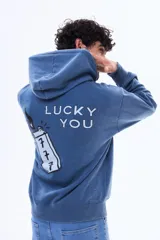 Buzo canguro oversize de felpa color azul, con capucha y estampa gráfica en la espalda que incluye la frase 'Lucky You' y un encendedor con el número 777.