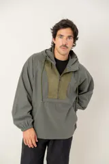 Canguro tipo anorak de color verde militar, con capucha ajustable y cierre frontal parcial. Presenta un panel central en contraste de textura gamuzada y un bolsillo frontal tipo canguro con solapa.
