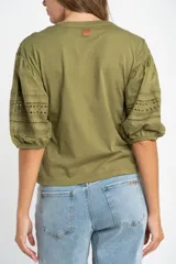 Remera de algodón color crudo con cuello redondo y mangas abullonadas de largo 3/4. Las mangas presentan detalles de encaje bordado y perforado con terminación elástica.