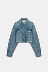 Sobrecamisa crop de denim con cuello solapa, manga larga con puños, bolsillos frontales con solapa y cierre de botones ocultos. Presenta un diseño con bajo deshilachado y detalles de roturas.