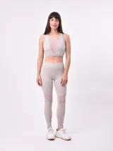 Top deportivo de color taupe con diseño de cuello redondo y panel central de malla transparente. Presenta un corte ajustado con banda elástica inferior para mayor soporte.