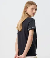 Remera negra de algodón con cuello redondo, manga corta y ribetes blancos contrastantes en cuello y mangas. Presenta una estampa fotográfica frontal de Jennie con tipografía en tonos rojos.