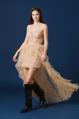 Falda larga de tul con diseño asimétrico, presentando una base corta y una sobrecapa voluminosa de volados en cascada que se extiende hacia atrás. Posee una cintura definida y un acabado etéreo.