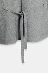 Jersey de punto color gris, con cuello redondo, mangas largas abullonadas con puños elásticos y cintura ajustable mediante cordón. Presenta una costura vertical marcada en la parte frontal.