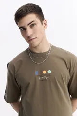 Remera de manga corta color verde militar, con escote redondo y un pequeño estampado frontal de formas geométricas de colores y texto manuscrito.