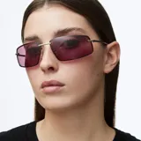 Lentes de sol con montura rectangular envolvente de acero inoxidable color plata y lentes de nylon color violeta. Presentan patillas de acetato y diseño inspirado en la estética de los años 2000.