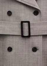 Chaqueta larga de lana color beige, con diseño recto, doble botonadura, cuello con solapa de muesca, trabillas en los hombros, manga larga, bolsillos laterales con solapa y cinturón ajustable con hebilla.
