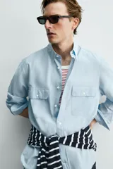 Camisa de corte relajado color celeste, confeccionada en mezcla de algodón y seda. Presenta cuello solapa, cierre frontal de botones, manga larga con puños abotonados y dos bolsillos de plastrón con solapa en el pecho.