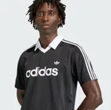 Remera polo Adidas Originals JSY negra con cuello blanco en V, tres rayas blancas en las mangas y logo Trefoil bordado. Confeccionada en tejido liviano y transpirable, con un corte regular.