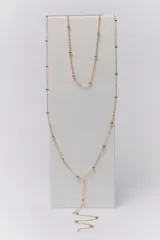 Collar dorado de doble cadena con pequeñas cuentas esféricas. El collar más corto llega a la clavícula y el más largo tiene un dije en forma de Y.