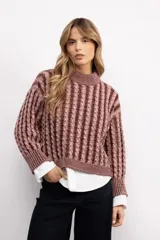 Sweater de tejido de punto con diseño de trenzas verticales, cuello alto y corte oversize. Presenta una textura marcada y puños acanalados.