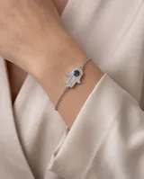Pulsera de cadena fina con dije central en forma de mano de Hamsa, decorado con pavé de cristales y un cristal central azul oscuro.