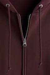 Campera con capucha de tejido pesado, color borgoña oscuro, con cierre frontal, bolsillos canguro y puños y bajo acanalados. Presenta un corte oversized y holgado.