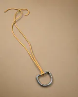 Gargantilla de cordón de cuero amarillo con dije de argolla metálica en forma de D.