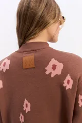 Sweater de tejido de punto color marrón con diseño estampado de flores en tonos rosados. Presenta cuello alto, mangas largas con puños ajustados y un corte relajado con terminación recta en la cintura.