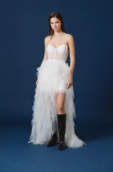 Falda larga de tul con diseño asimétrico, presentando una base corta y una sobrecapa voluminosa de volados en cascada que se extiende hacia atrás. Posee una cintura definida y un acabado etéreo.
