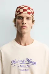Camiseta de corte boxy fit, color beige con efecto lavado, cuello redondo y manga corta. Presenta un estampado gráfico en azul oscuro en el frente con tipografía estilo vintage.
