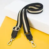 Correa de tela negra con franjas color beige, terminaciones en cuero sintético negro y mosquetones metálicos plateados.