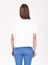 Remera de manga corta color beige claro, con cuello redondo y estampado floral en tonos dorados y plateados. Las mangas tienen un detalle de tejido acanalado.