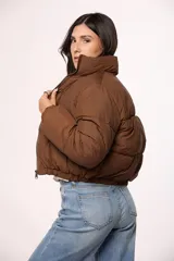 Campera tipo puffer de corte corto y diseño acolchado, con cuello alto y cierre frontal completo. Presenta un acabado liso en color marrón y ajuste elástico en la cintura.