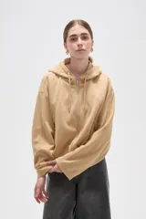 Campera de suede color beige con capucha, cierre frontal completo y mangas largas. Presenta un diseño holgado con bolsillos laterales y detalles de frunces en el ruedo.