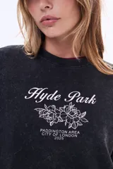 Buzo de felpa con cuello redondo, corte holgado y mangas largas. Presenta un efecto de lavado gastado en color negro y una estampa frontal con texto y diseño floral.