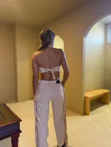 Pantalón de gamuza color beige con flecos en los laterales, tiro alto y corte recto.