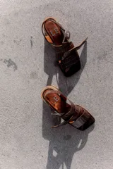 Sandalias de cuero negro con textura de reptil, diseño de punta cuadrada y taco bloque de madera. Presentan tiras cruzadas en el empeine y una hebilla metálica grande decorativa.